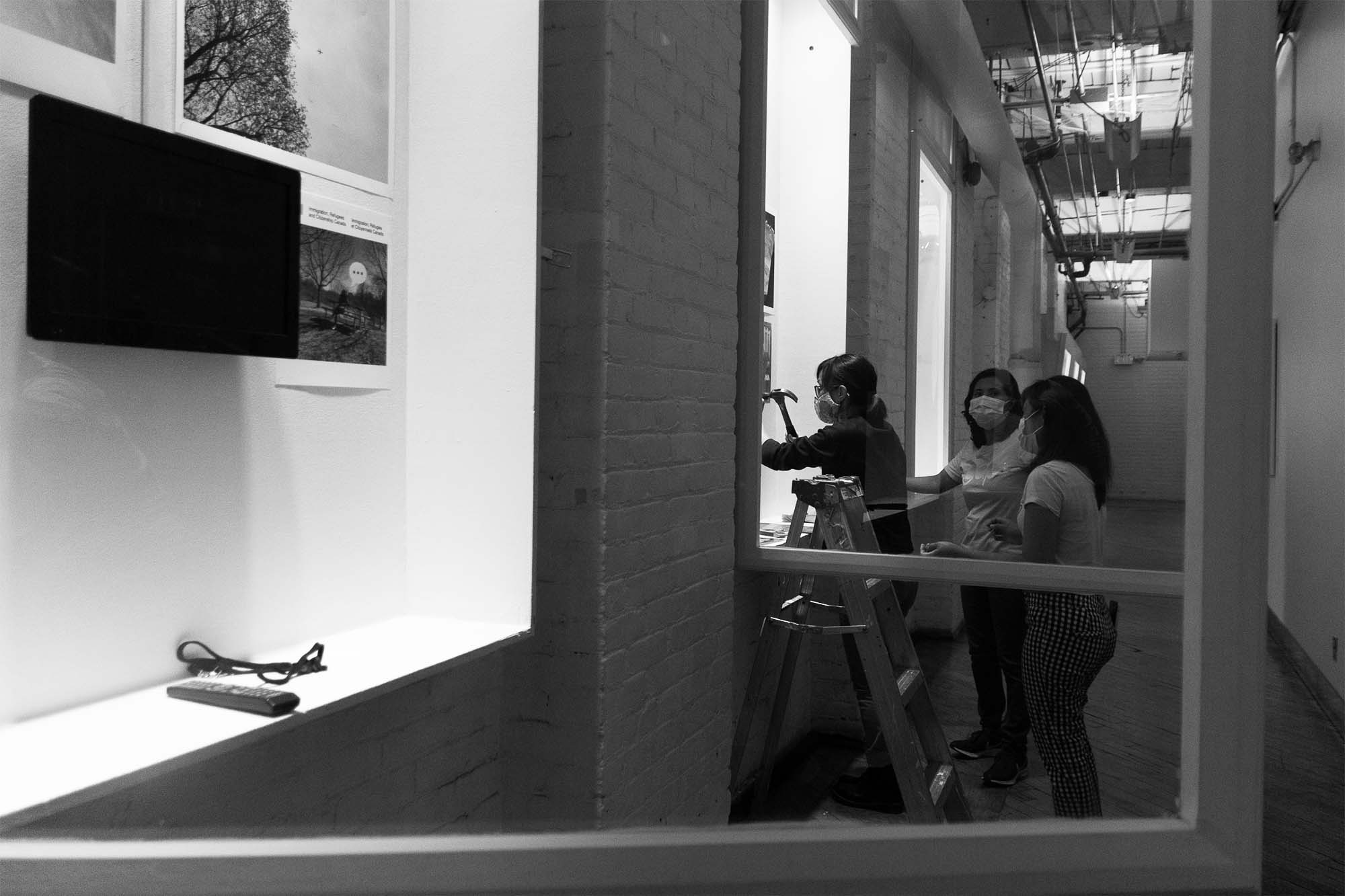3 people installing exhibition in A Space gallery windows